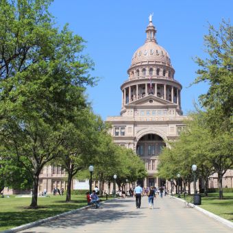 State capitol building surrounded by trees with people walking toward the structure
