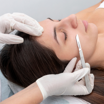 Professional holding a dermaplaning tool to a woman's cheek
