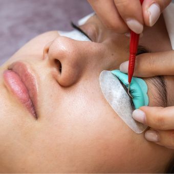 Woman receiving lash lift service from an esthetician who is holding an eyelash implement