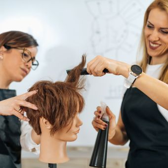 Cosmetology instructor overseeing a cosmetology student practice haircutting skills on a mannequin with short hair