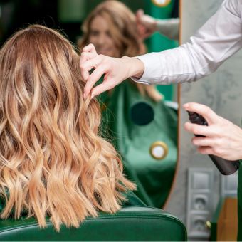 Cosmetologist sparying hairspray onto curly blonde hair