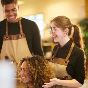 Two cosmetologists observe a hairstyle of a client with curly hair