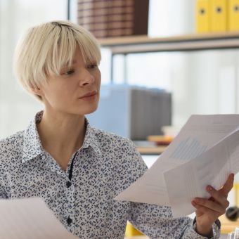 Man with blonde hair wearing blue and white patterned shirt reviewing documents